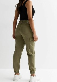 Pantalons cargo vert olive avec une taille élastique, ourlets à poignets, poches latérales et poches arrière, fabriqués dans un tissu léger.