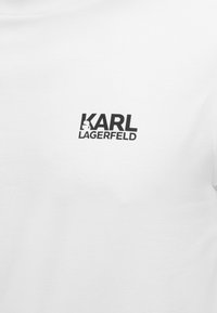 Λευκό ύφασμα με μαύρο λογότυπο κειμένου «KARL LAGERFELD», που περιλαμβάνει μια μικρή σιλουέτα του προφίλ του Karl Lagerfeld μέσα στο γράμμα «K».