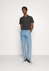 Zwart polo shirt met een gele logo, gecombineerd met lichtblauwe rechte jeans en zwarte hoge sneakers. Eenvoudig ontwerp, gemaakt van katoen.