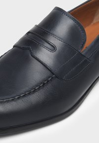 Mocassino in pelle blu navy con design cucito e una fascia rialzata con decorazioni a intaglio; finitura liscia e punta arrotondata.