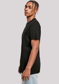 Schwarzes Baumwoll-T-Shirt mit kurzen Ärmeln, Rundhalsausschnitt und lässiger Passform, an einem Modell im Profil präsentiert. Einfache und glatte Textur.