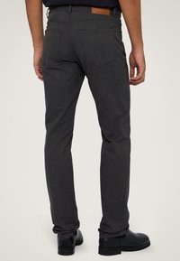 Grijze broek met een slim fit, voorzien van platte achterzakken en een leren label op de tailleband. Het materiaal lijkt soepel en duurzaam.