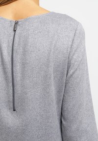 Grå ullblandad topp med rund halsringning, långa ärmar och dragkedjedetalj i mitten bak. Slät yta med subtilt fleeceaktig finish.