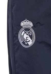 Tela azul marino con un escudo bordado en blanco del Real Madrid, con una corona, diseño circular y letras entrelazadas. Superficie texturizada.