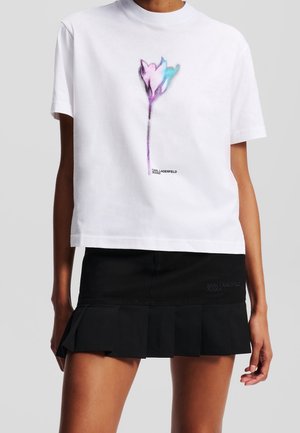 T-shirt blanc à manches courtes avec un motif abstrait de fleur violette et bleue et mini-jupe plissée noire avec broderie subtile du logo.