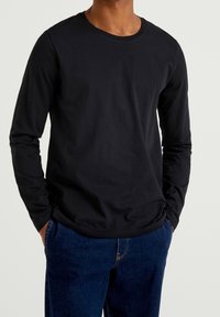 Camiseta de manga larga negra hecha de suave tela de algodón con cuello redondo. Presenta un ajuste relajado y un diseño sencillo. Combinada con jeans azul oscuro.