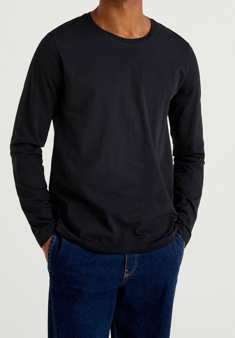 Camiseta de manga larga negra hecha de suave tela de algodón con cuello redondo. Presenta un ajuste relajado y un diseño sencillo. Combinada con jeans azul oscuro.