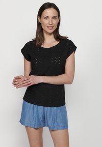 Černý top s krátkým rukávem s designem očí, kulatým výstřihem, texturovanou látkou a volným střihem, spárovaný s denimovými šortkami.