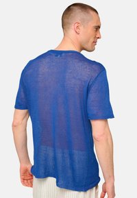 Blue knitted short-sleeve shirt with a loose fit, textured fabric, and unfinished hems, revealing a see-through design.