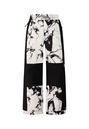 Jeune personne portant un pantalon de neige noir et blanc à motifs, un haut noir à manches longues, des bottes noires et un bonnet d'hiver noir avec des lunettes de ski.