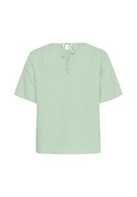 Camicetta verde chiaro a maniche corte con una finitura testurizzata e un nastro sul retro del collo. Vestibilità rilassata con un design semplice e minimalista.