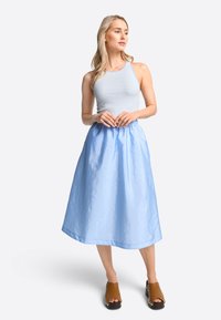 Helles Blaues, knielanges Kleid mit einem gerafften Taillenbund und glatter Textur, kombiniert mit einem grauen gestreiften, figurbetonten Tank-Top und braunen Holzclogs.