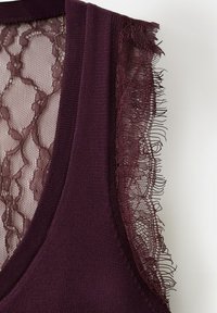 Gros plan sur un haut sans manches violet foncé avec un bord en dentelle florale festonnée sur l'épaule et un panneau arrière en dentelle transparente.