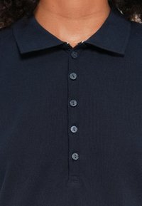 Dunkelblaues Poloshirt aus strukturiertem Stoff, mit einem Kragen, fünf Knöpfen und einer sauberen Verarbeitung ohne sichtbare Logos oder Muster.