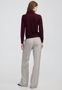 Bordowy sweter z golfem w połączeniu z jasnoszarymi, dopasowanymi spodniami z subtelnym wzorem w kratę i bocznymi kieszeniami. Gładka tekstura.