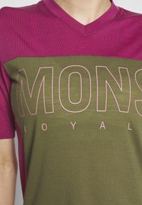 Tričko s krátkým rukávem a výstřihem do V, s vínovým horním dílem a olivově zeleným dolním dílem, s velkým růžovým textovým logem.