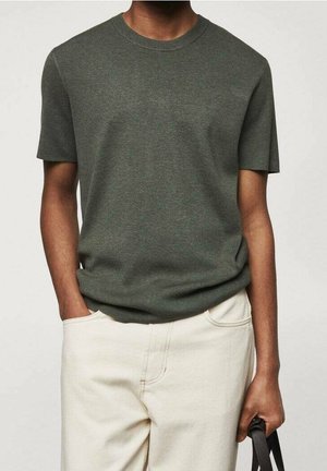 Dunkelgrünes T-Shirt mit kurzen Ärmeln aus einem weichen Strickstoff; Rundhalsausschnitt; getragen zu hellen Hosen; legerer Schnitt.