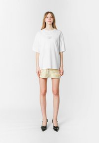 Camiseta blanca de gran tamaño con un pequeño logo, combinada con pantalones cortos amarillos texturizados con un patrón de bloques, complementada con tacones negros de punta.
