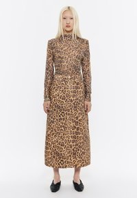 Top a maniche lunghe con stampa leopardata e gonna maxi coordinata, entrambi in beige con macchie marroni scure; texture liscia; abbinato a scarpe basse nere.