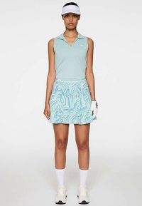 Una polo azzurro chiaro senza maniche con colletto e una gonna plissettata coordinata con un motivo geometrico in varie tonalità di blu.