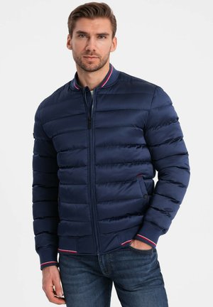 Marineblauer Pufferjackett mit horizontaler Steppstruktur, geripptem Kragen mit rot-weißen Akzenten und seitlichen Taschen mit Druckknopfverschluss.