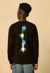 Must mustärge pikkade varrukatega T-särk, mille seljal on värviline graafikatekst sinise, rohelise ja valge värviga, lõdva lõike ja soonikute varrukatega.