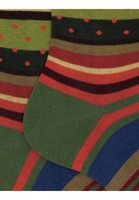 Due calzini colorati con righe verdi, rosse, blu e marroni, e pois rossi su uno sfondo verde scuro.