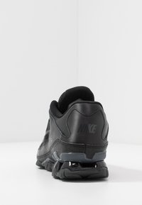 Black Nike shoes featuring a textured mesh and synthetic upper, cushioned heel, and a sleek, curved sole with prominent branding.