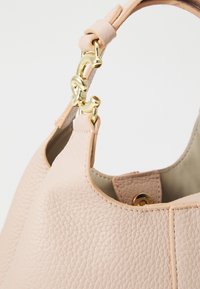 Light pink leather handbag with a textured finish. Features a gold hardware clasp and a smooth inner lining. Shape is rounded with an open top.
