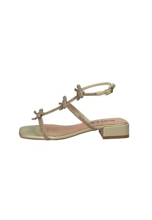 Sandalo piatto beige con punta quadrata, tre sottili cinturini decorati con piccoli fiocchi, cinturino alla caviglia con fibbia e tacco basso a blocco.