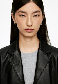 Black leather blazer over a gray t-shirt. Blazer features a notched lapel and smooth texture. Model has straight, long dark hair.