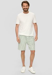 Weißes T-Shirt mit Rundhalsausschnitt, kombiniert mit hellgrünen gestreiften Shorts. Die Sneakers sind weiß. Der Stoff scheint weich mit einem lockeren Schnitt zu sein.