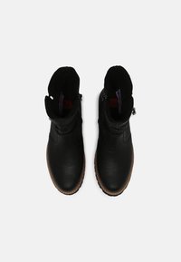 Botas de tobillo de cuero negro con un puño de tela texturizada, cremalleras laterales y suelas de goma marrón. Diseño minimalista con un acabado suave.