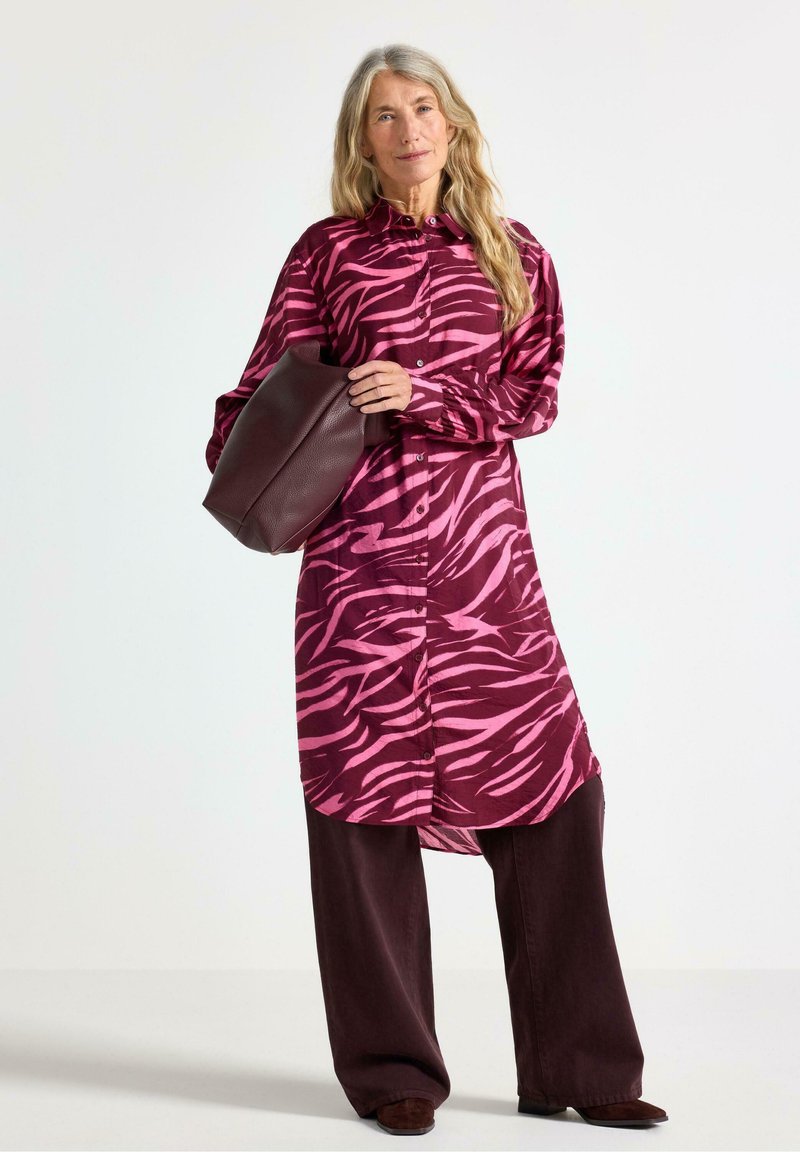 Långärmad skjortklänning med ett rosa och vinrött zebramönster, knappframsida och tillsammans med mörk vinröda vida byxor.