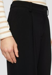 Zwarte op maat gemaakte broek met een zachte textuur, voorzien van een platte voorkant, zijzakken en een knoopsluiting bij de tailleband.