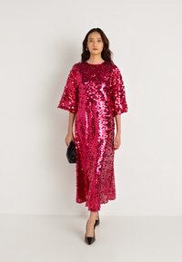 Μαγεντα φορεμα με παγιέτες, μισά μανίκια και με ίσια γραμμή, σε συνδυασμό με μια μαύρη τσάντα φάκελο και ψηλοτάκουνα παπούτσια.