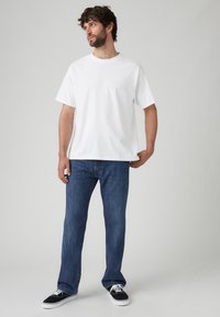 Camiseta blanca de algodón con mangas cortas, combinada con jeans de mezclilla azul oscuro. El calzado consiste en zapatillas de lona negras con suelas blancas.