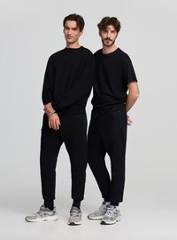 Felpa nera e t-shirt abbinate a pantaloni jogger neri. Tessuto morbido, vestibilità rilassata, tasche con cerniera e stile con sneaker grigie.
