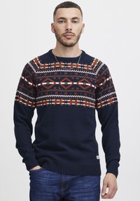 Pulover tricotat bleumarin cu un model geometric în roșu, alb și portocaliu. Include manșete și tiv cu nervuri; guler rotund.
