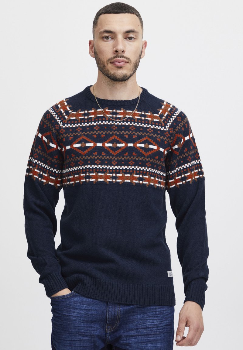 Pulover tricotat bleumarin cu un model geometric în roșu, alb și portocaliu. Include manșete și tiv cu nervuri; guler rotund.