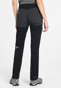 Svarta utomhusbyxor med en grå bakpanel, som har en ficka med dragkedja på sidan och en figursydd design. Klasar ihop med grå, strukturerade skor.