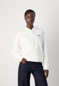 Vit hoodie med huva, framficka och grön broderad logotyp. Slät yta, avslappnad passform, med ribbade muddar och nederkant.