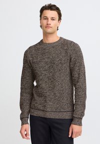 Brown and cream textured sweater in a chunky knit design with a crew neckline and ribbed cuffs and hem, paired with black pants.
