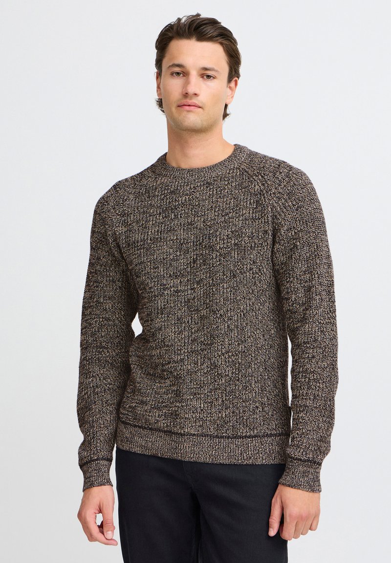 Brown and cream textured sweater in a chunky knit design with a crew neckline and ribbed cuffs and hem, paired with black pants.