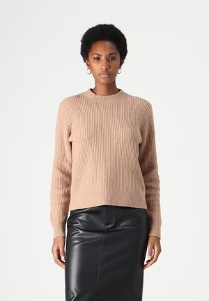 Beige knitted sweater with a ribbed texture, crew neckline, and long sleeves, paired with a black leather skirt.