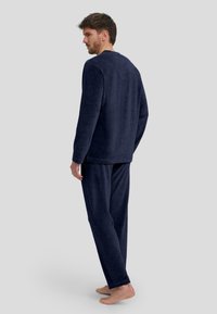Conjunto de loungewear de felpa azul marino que incluye una camiseta de manga larga de corte relajado y pantalones de pierna recta, con una textura suave y un diseño minimalista.