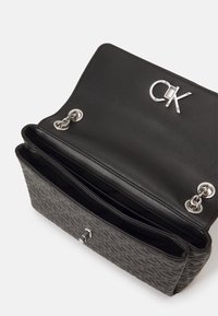 Borsa nera con un design texturizzato, accessori in argento e un accento con logo. L'interno presenta diversi scomparti.
