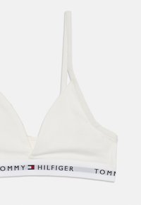 Balta medvilninė braletė su trikampio formos dizainu ir plonomis petnešėlėmis. Dėl horizontalios juostos su juodu ir raudonu tekstu "TOMMY HILFIGER".