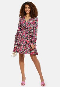 Blumenkleid mit lebhaften pinken, lila und grünen Mustern, langen Ärmeln, gerafftem Saum und einem gebundenen Taillendetail.