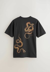 Must lühikeste varrukatega T-särk, mille tagaküljel on kaks suurt oranži keerutatud madu trükitud, üks õla juures ja teine allosas.